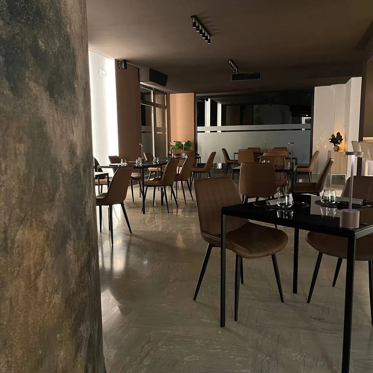 La sala di Numen di giorno, con i tavoli neri, le sedie in pelle color cognac e la parete dipinta.